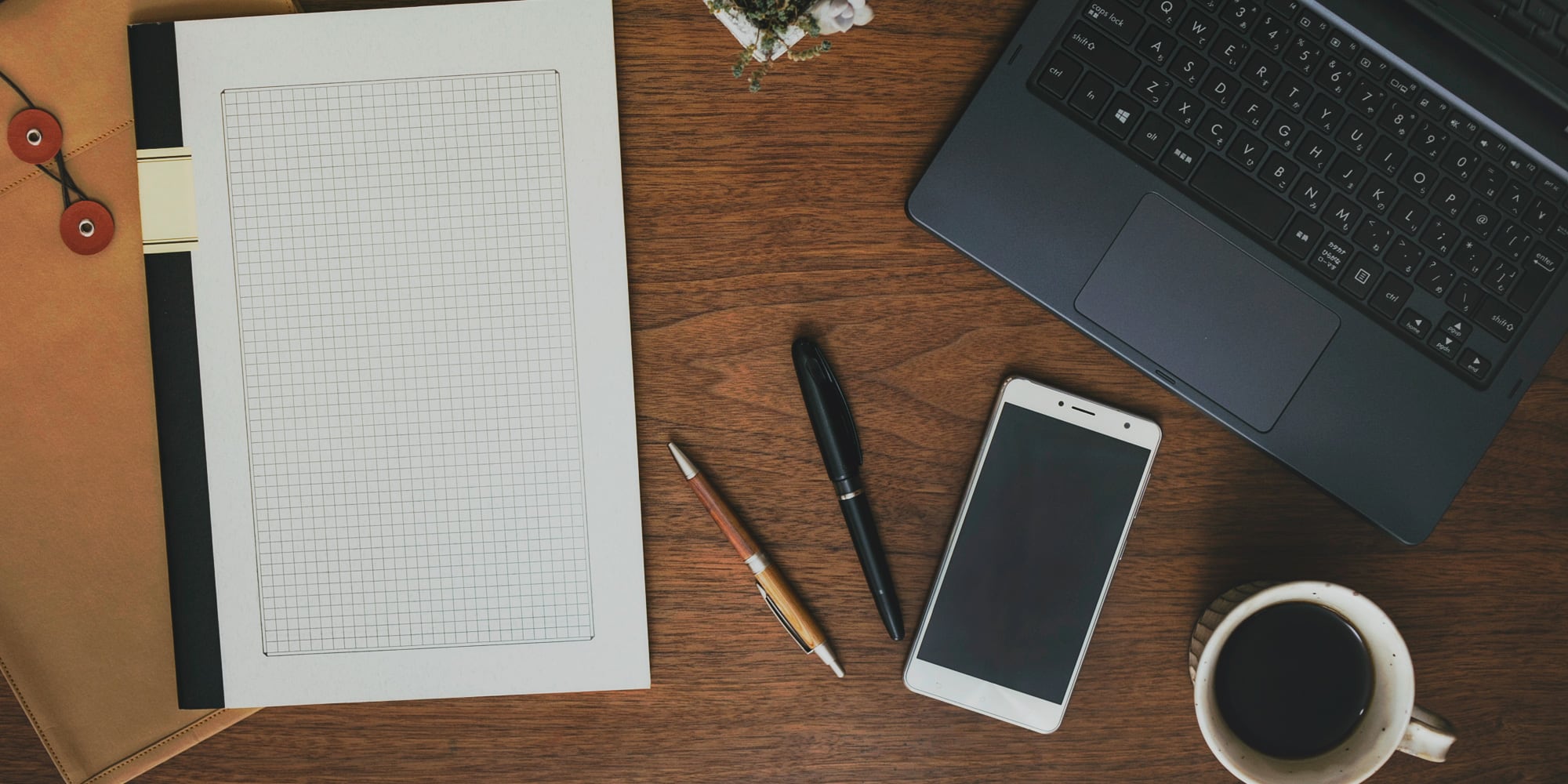 デスク上のノート・ノートPC・スマートフォンが並ぶ写真